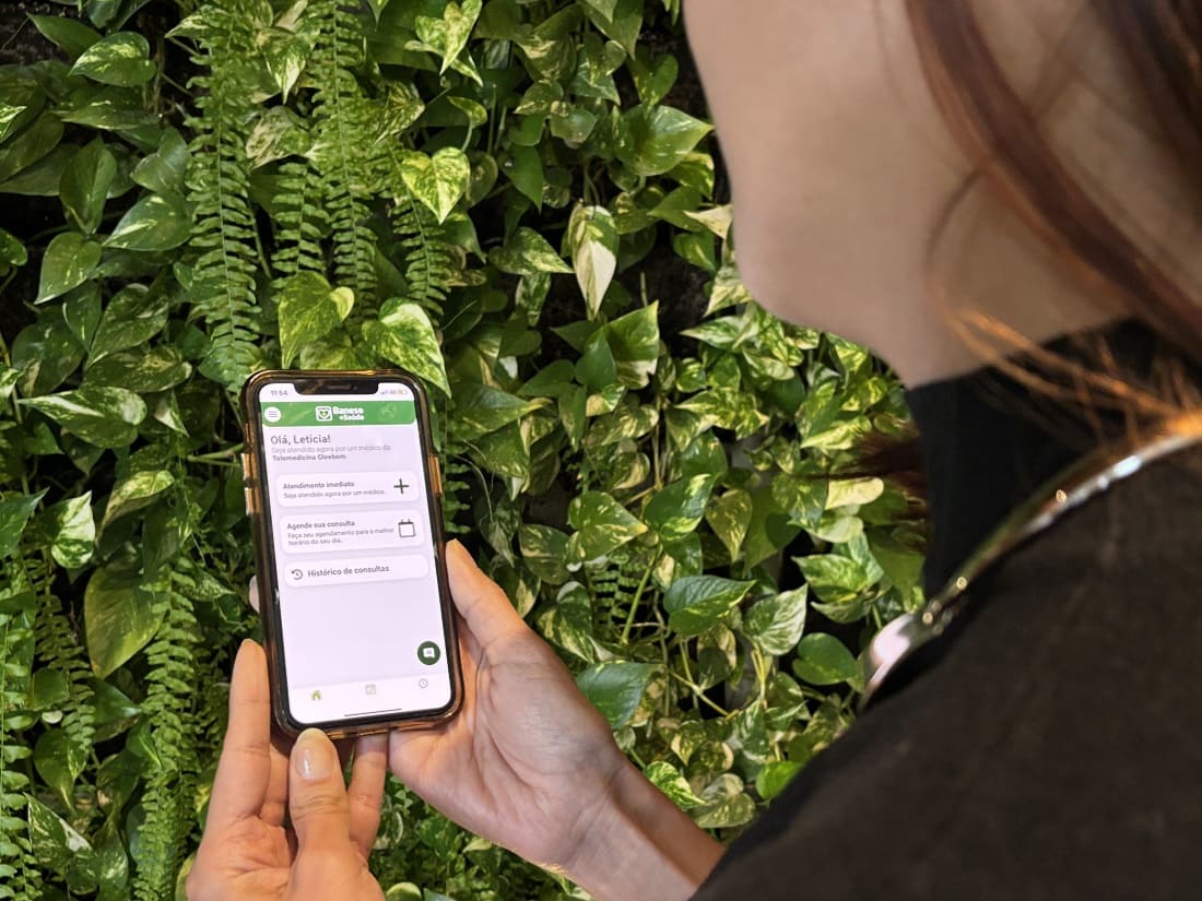 Mulher segurando o celular com app na tela da Gleebem Banese +Saúde 