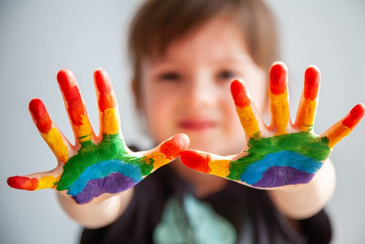 Criança com as mãos pintadas com as cores do autismo