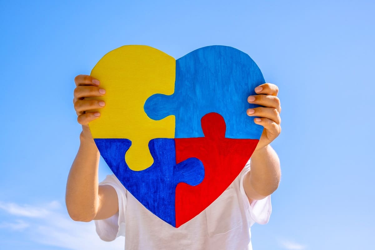 Criança segurando coração com as cores do autismo
